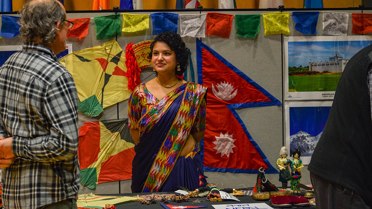 Displayed are several images of Nepal, as well as Buddhist prayer flags, the flag of Nepal and kites. Also featured are figurines dressed in traditional Nepalese attire, along with other small cultural items such as game pieces and shoes.  