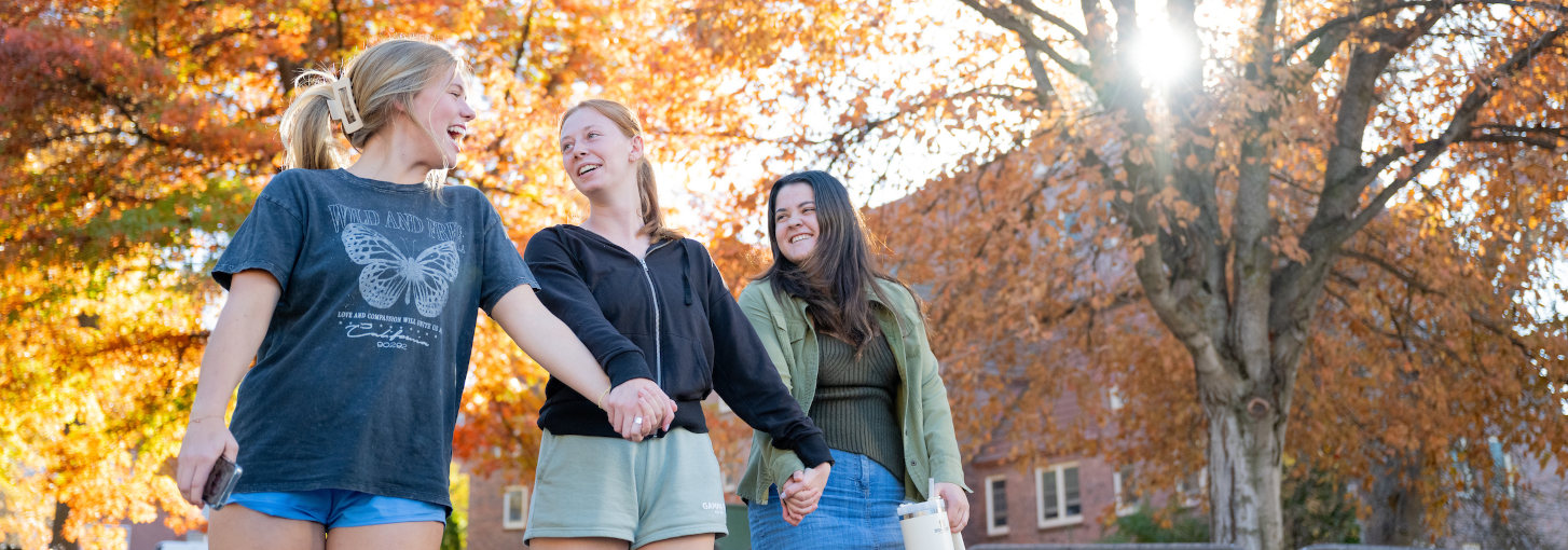 A group of students walk hand in hand on campus.