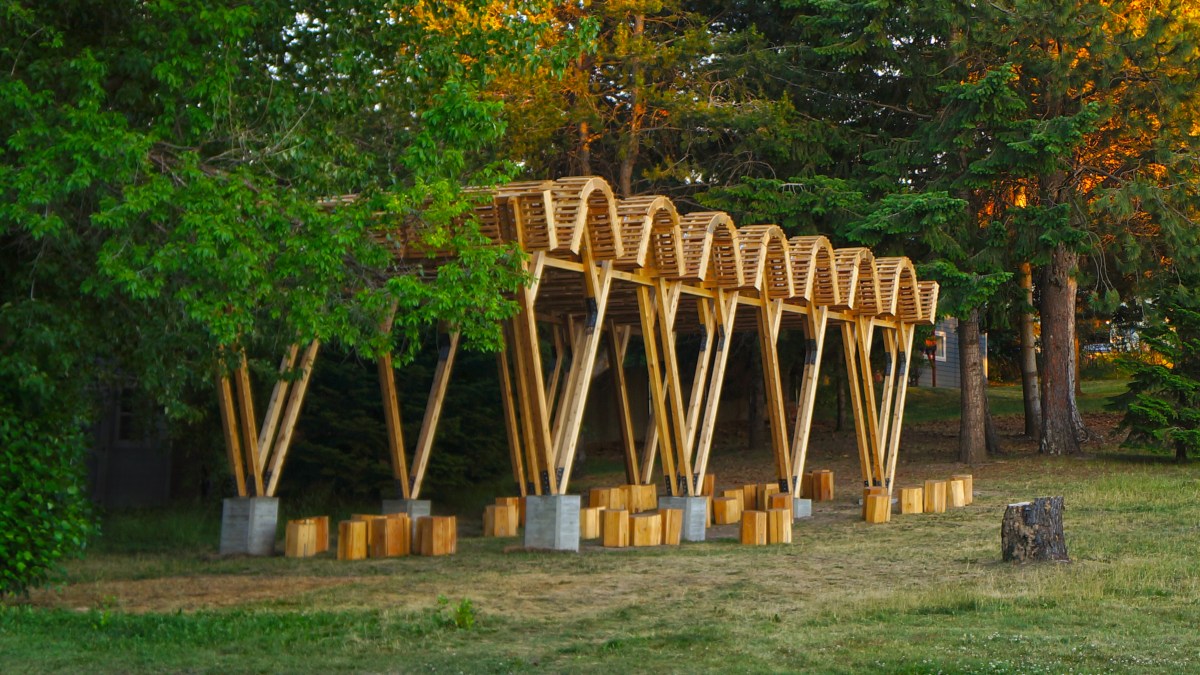 A rolling roof and V-shaped framed outdoor classroom sits before trees.