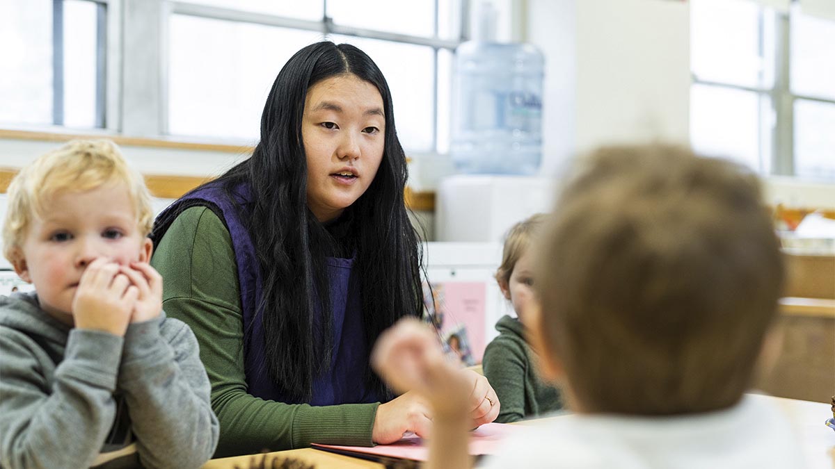 A woman sits at a table with a group of young children.