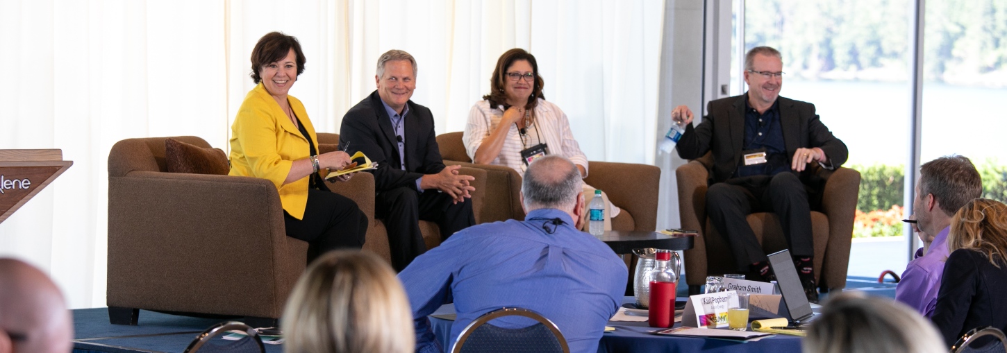 Four panelists seated in armchairs address Energy Executive Course participants seated around refreshment tables.