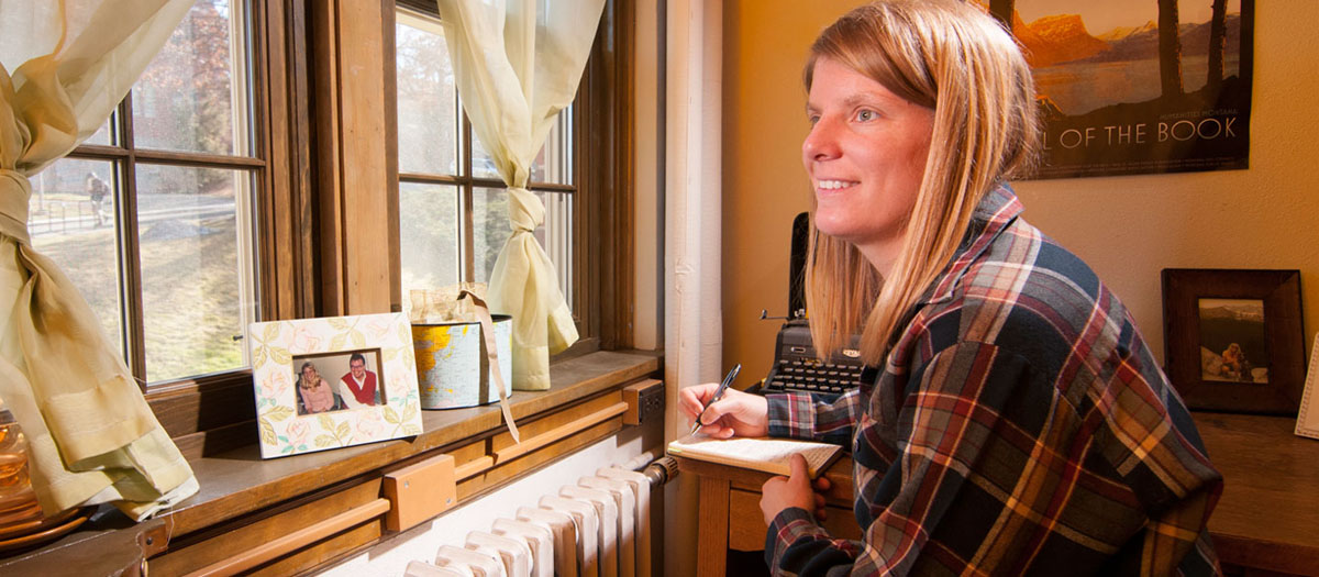 A graduate student writing at her desk in Brink Hall