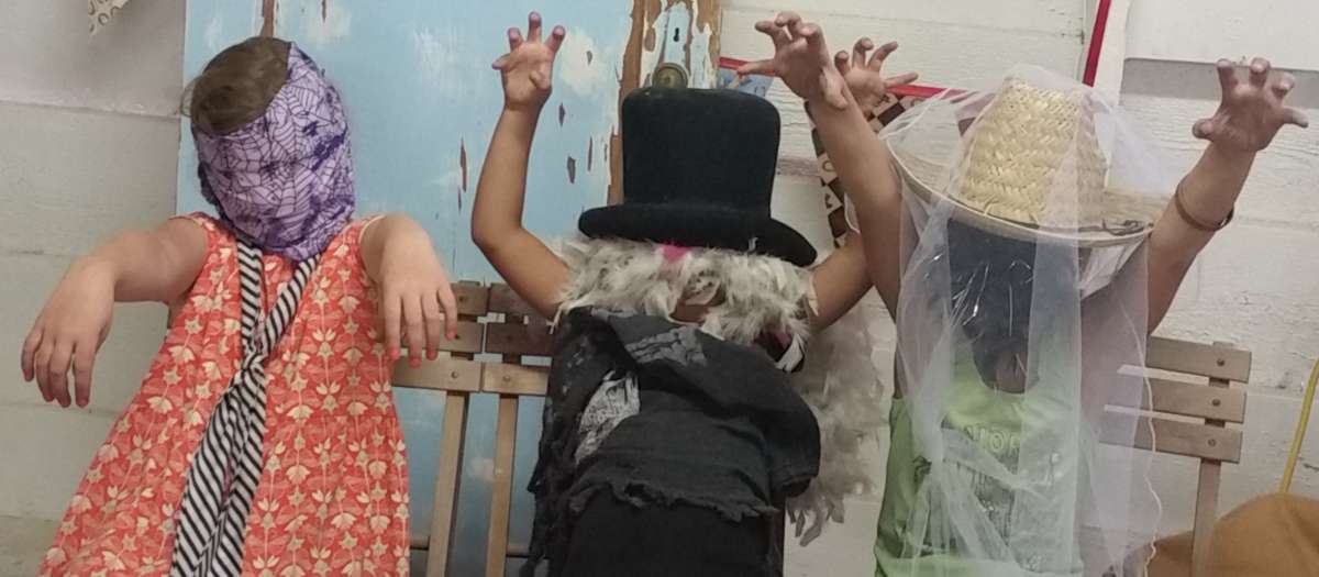 Three kids dressed in costumes make scary monster gestures.