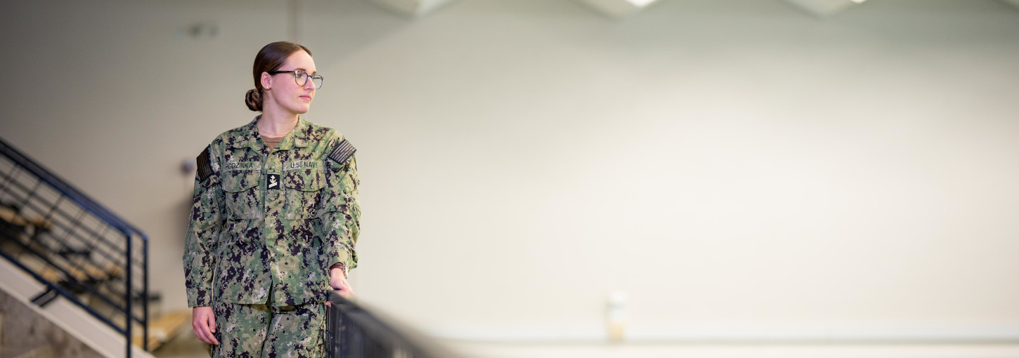 Woman wearing battle dress uniform stands near swimming pool.