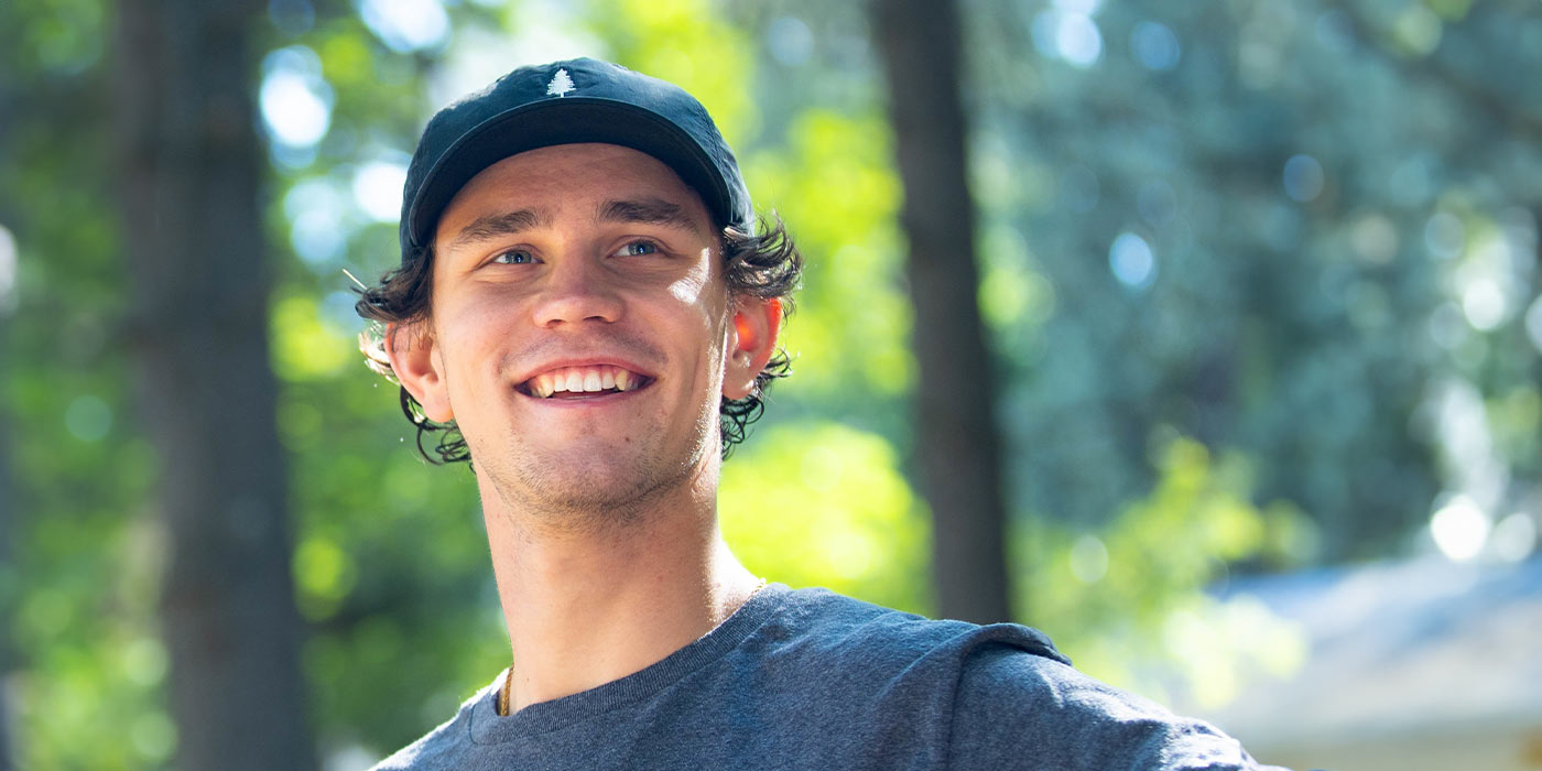 A portrait of James Stone standing in a sun lit evergreen forest